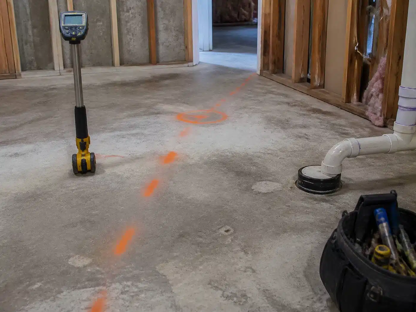 Wider view of the work area, electronic pipe locator and chalk marks tracing a buried drain line under a Denver basement slab