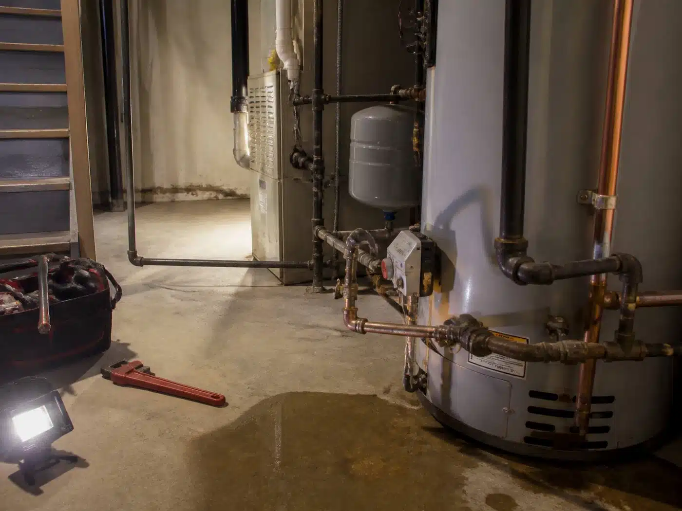 Wider view of the work area, licensed plumber working an emergency call by work light in a Denver basement