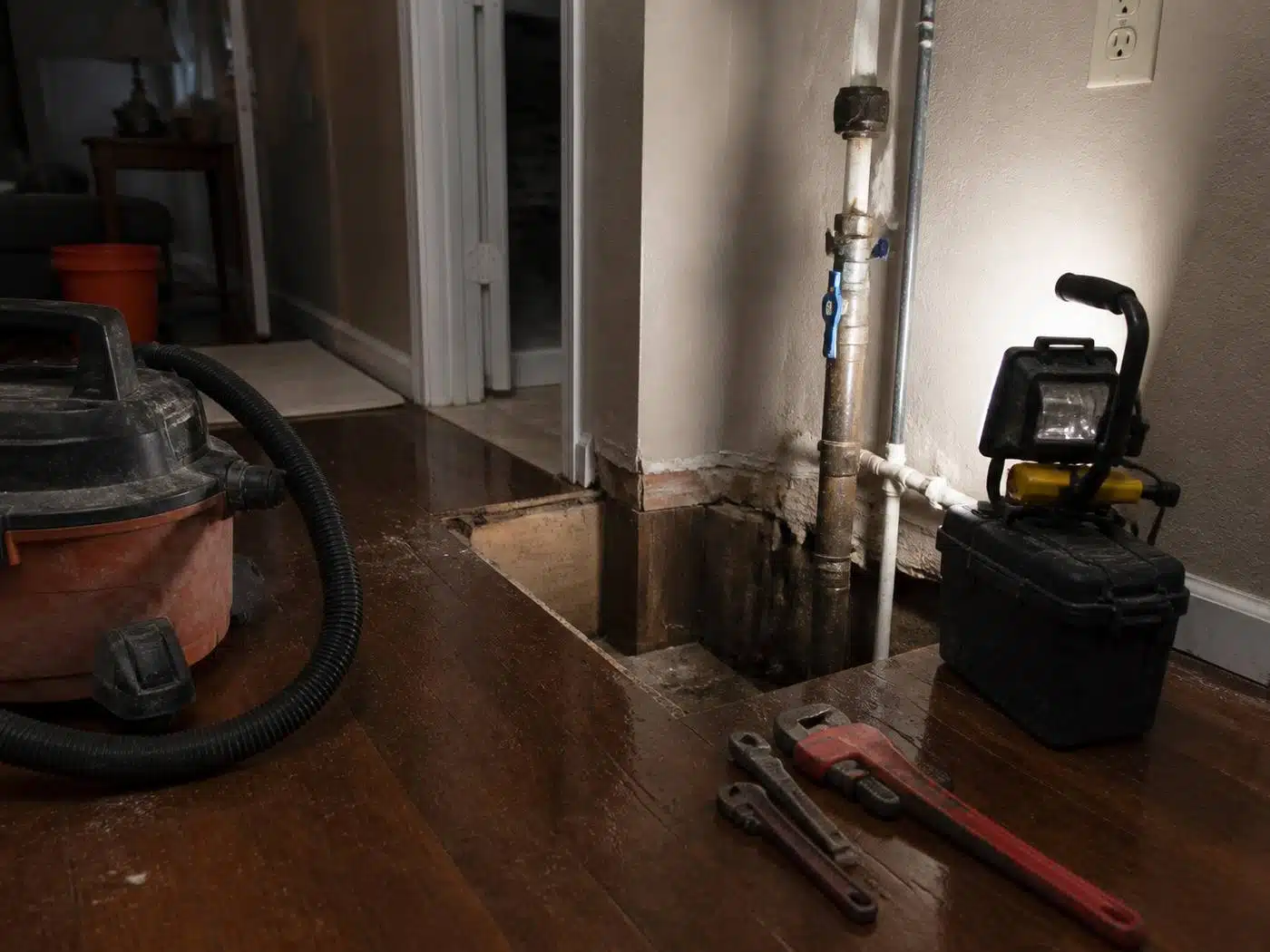 Wider view of the work area, after hours emergency plumbing setup in a Denver home with work light, wet vacuum, and pipe wrenches staged at a shut-off valve
