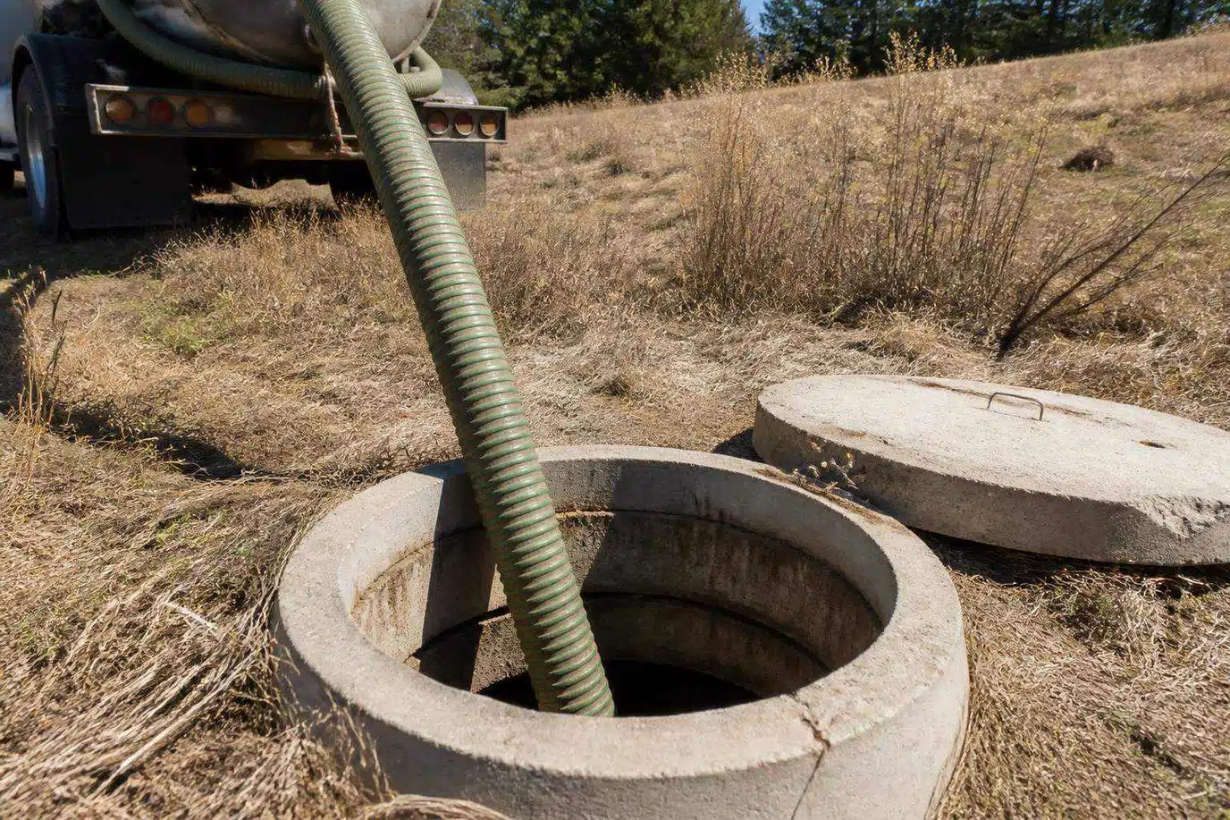 Septic tank pumping on a Colorado property with a heavy vacuum hose lowered into an exposed concrete tank riser