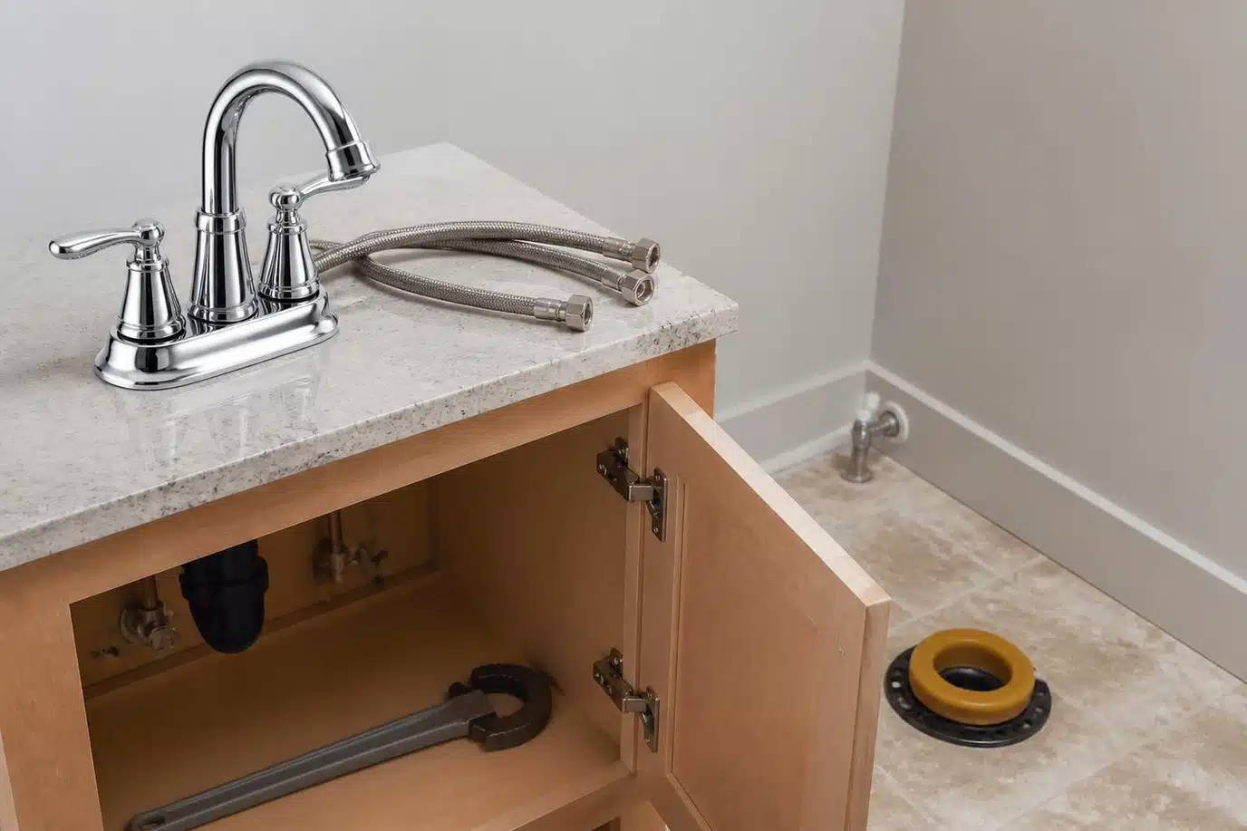 Sink faucet and toilet replacement in progress with a new chrome faucet, braided supply lines, and a fresh wax ring at the closet flange